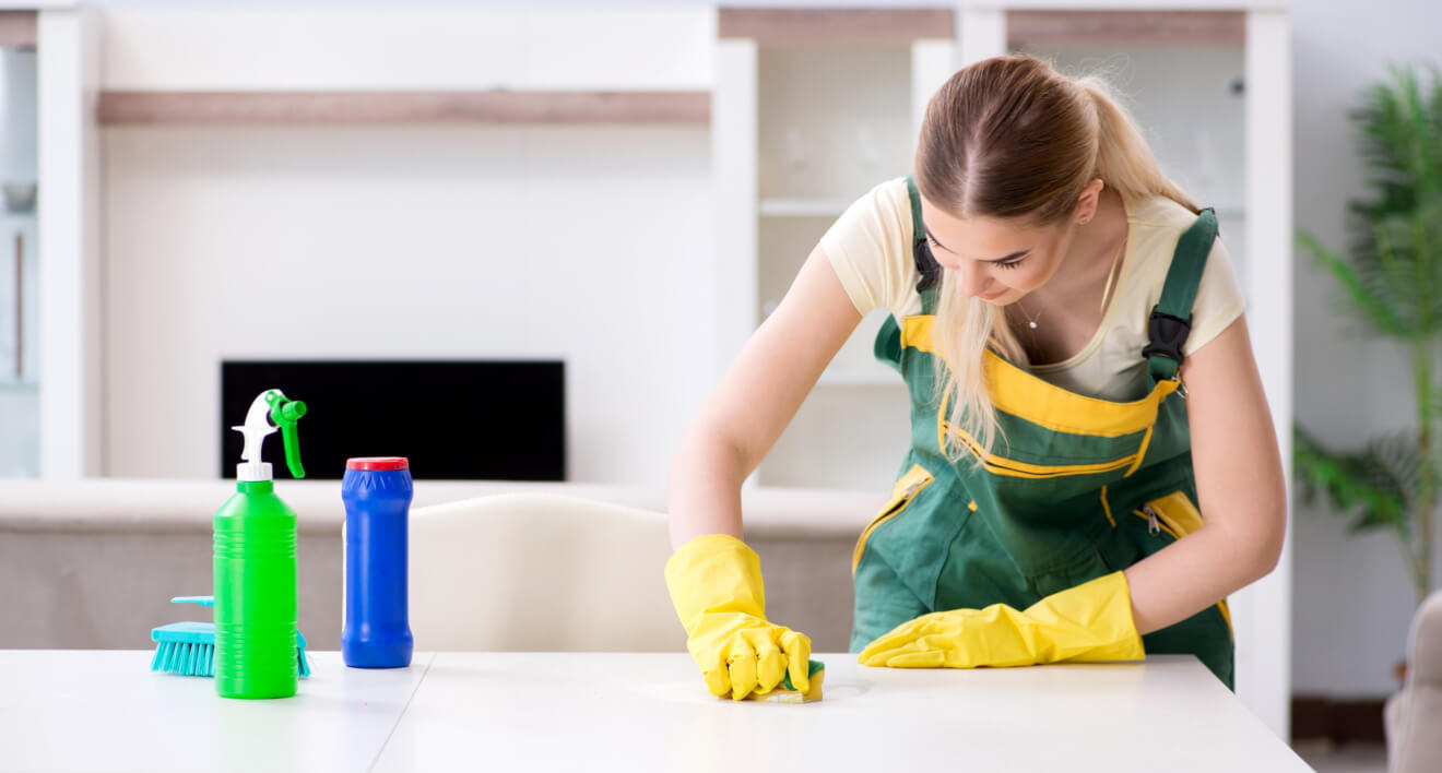 Cleaner wiping a kitchen worktop beside cleaning supplies.