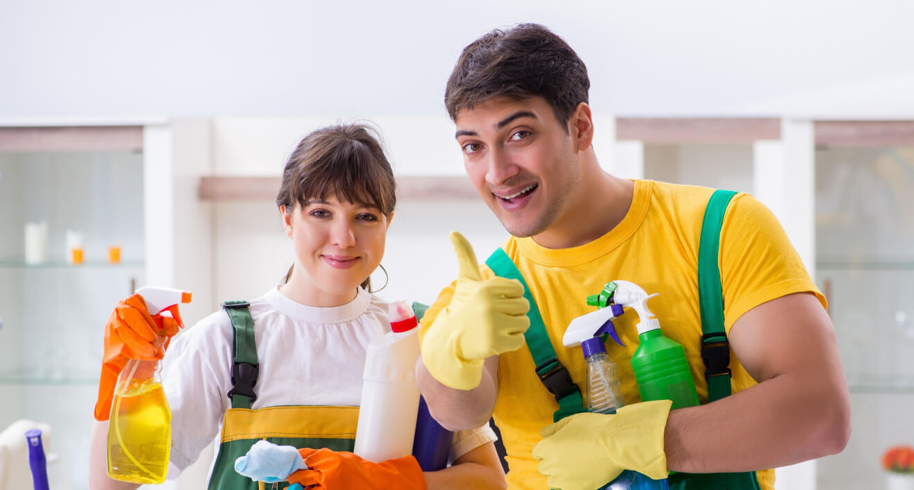 Two cleaners holding cleaning supplies in a kitchen.