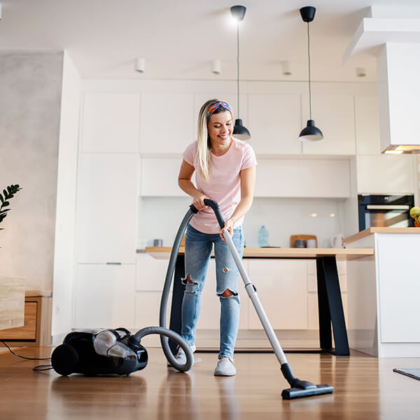 Woman vacuuming a kitchen floor.