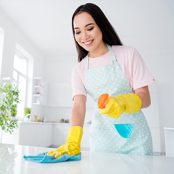 Cleaner wiping a kitchen countertop with a cloth and spray bottle.