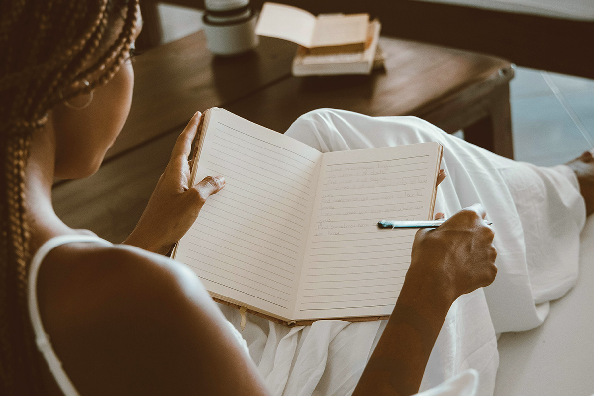 Black woman takes time for self care to journal. Soft caml setting symbolic of prioritizing mental health.