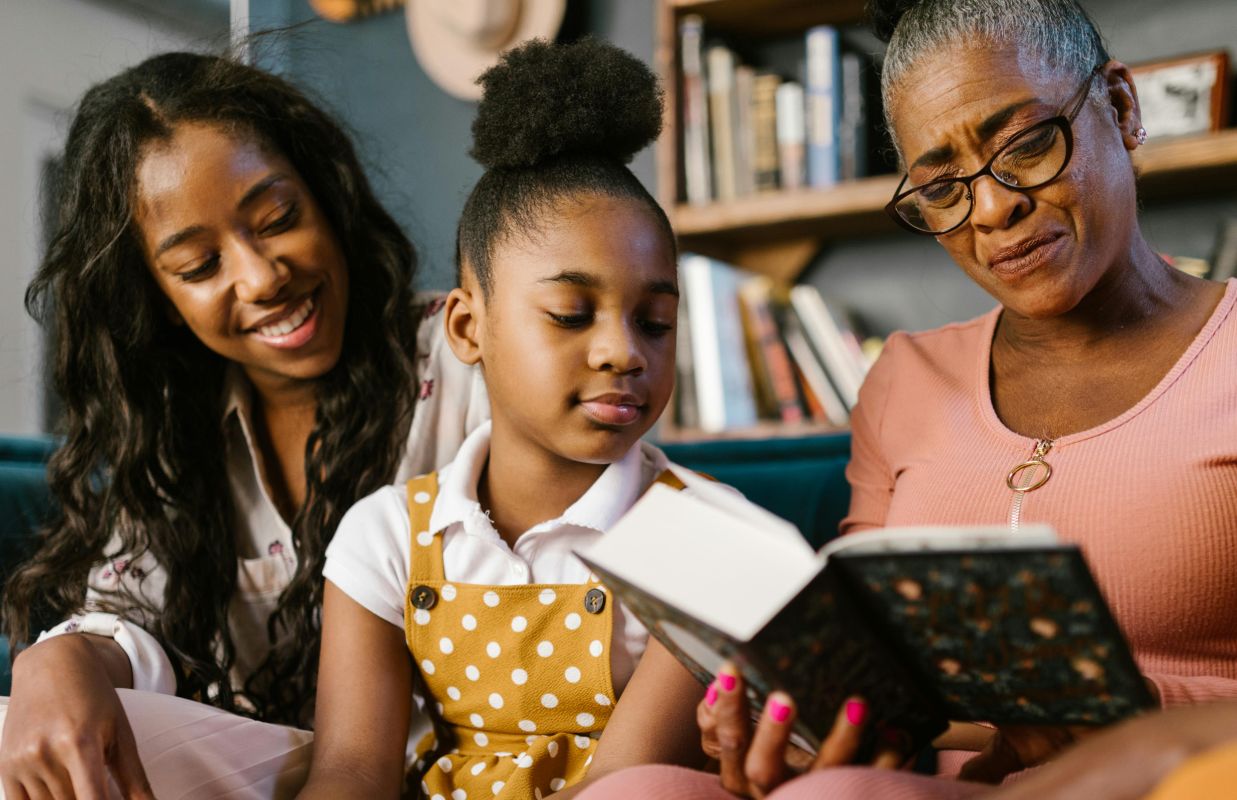 Generational black family enjoying a book together symboliizing cultural identitiy and strong bonds as nuturing resilience and neuroplasticity.