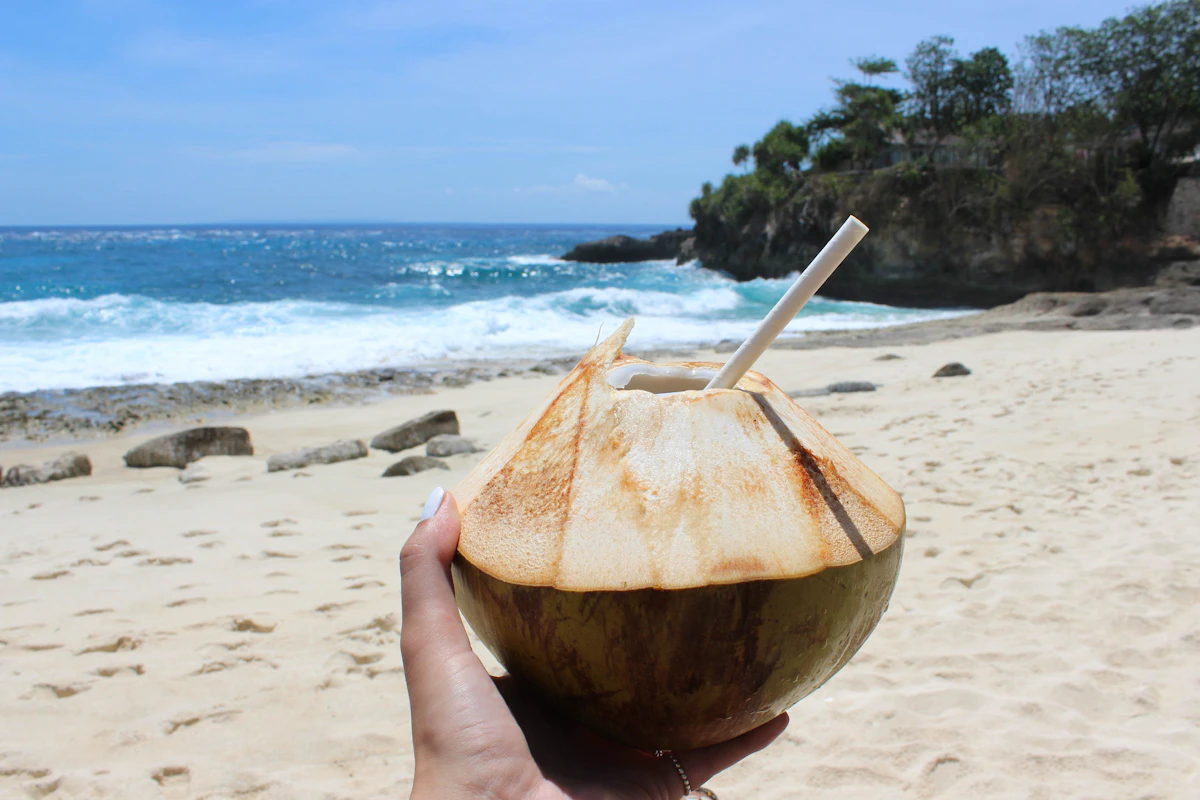 Fresh coconut with a straw held up on a beach in Bali