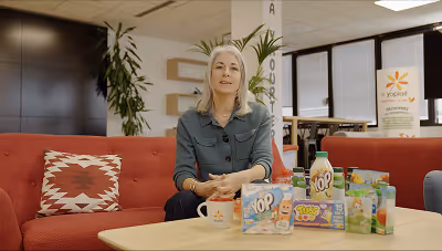 Femme assise sur un canapé rouge avec des produits alimentaires et des boissons sur une table devant elle dans un bureau moderne.