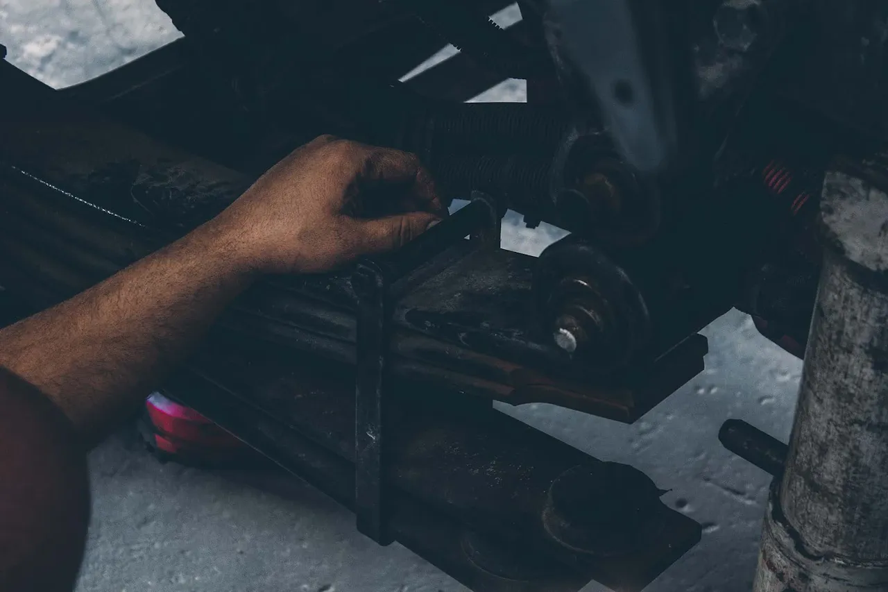 Suspension repair as a technician inspects a heavy-duty leaf spring and shackle assembly beneath a truck trailer.