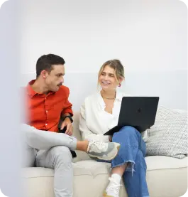 Man and woman sitting on a couch looking at each other, woman holding a laptop on her lap.