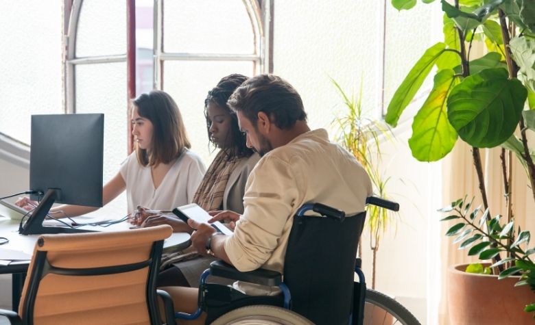 Graphic showing three colleagues working together in an office, including a man using a wheelchair, highlighting workplace diversity and inclusion.