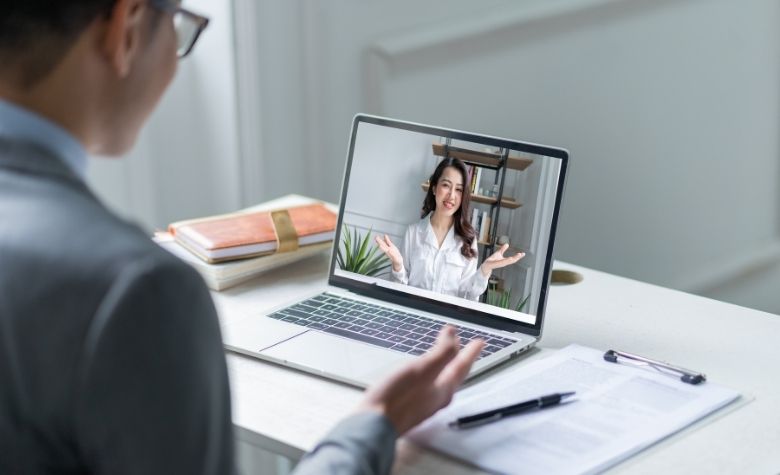 Graphic showing a virtual job interview, with a candidate speaking on a laptop screen, representing modern talent acquisition strategies for attracting global talent.