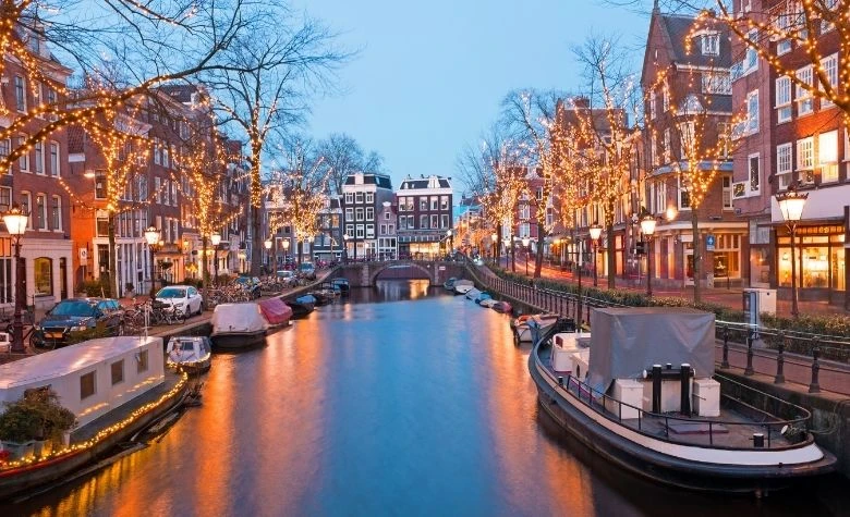 Graphic showing Amsterdam canal lined with historic Dutch buildings at dusk, representing a rich and established talent pool which can be compensated through partnering with payroll service providers in the Netherlands for 2026. 