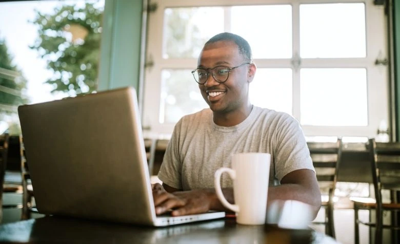 Graphic showing a smiling professional working on a laptop in a bright café setting, representing remote work and global digital employment opportunities in Africa.