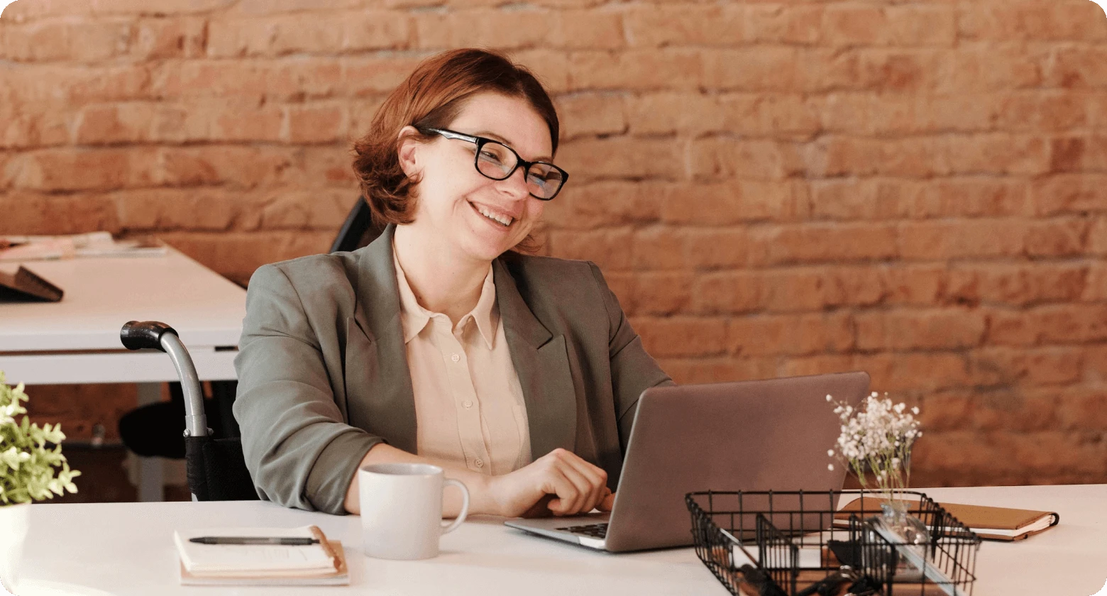  Professional woman with a disability smiling while working on her laptop, highlighting remote work benefits.