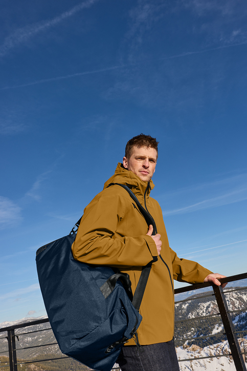A man standing with a large bag in front of snowy mountains