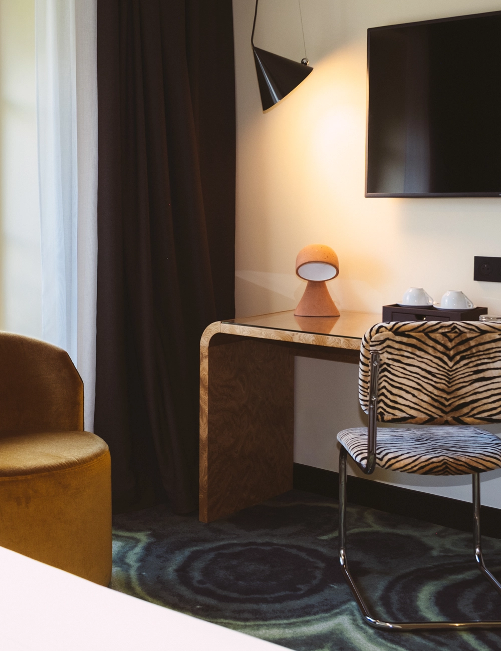 Modern corner with wood desk, tiger-striped chair, yellow armchair, wall lamp, and TV.