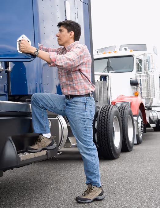 Truck driver stepping into a blue semi-truck in front of another truck – Our Mission section
