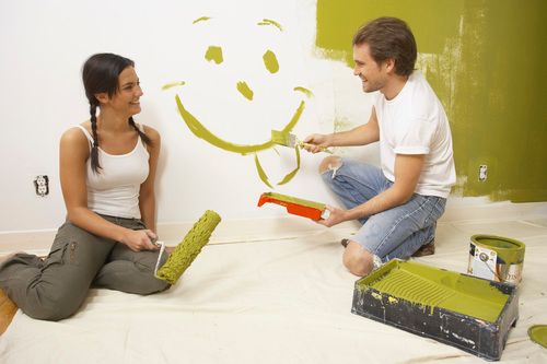 A man and female paint a wall with a smiley face 