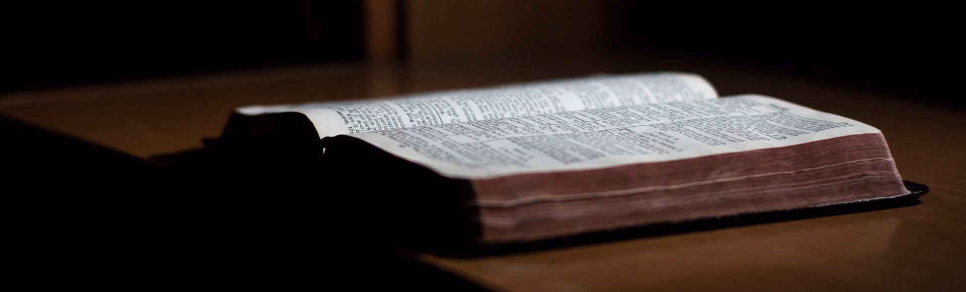 Bible ouverte posée sur une table en bois avec un fond sombre.