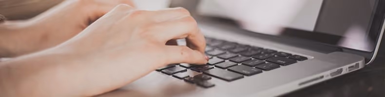 Mains tapant sur le clavier d'un ordinateur portable gris foncé.