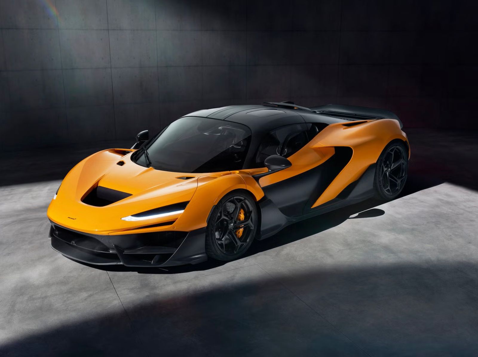 A papaya orange McLaren supercar in a dark studio