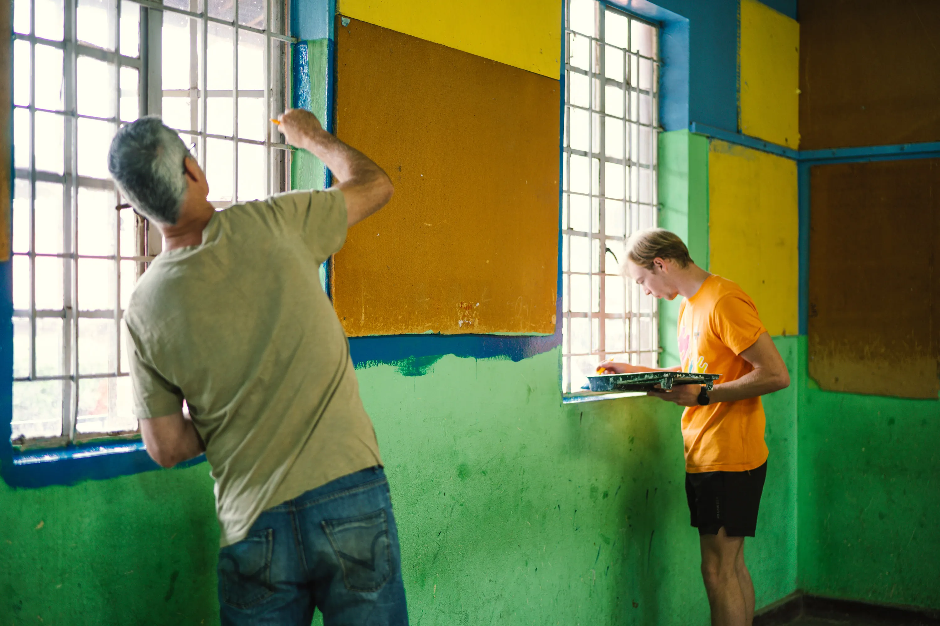 Two volunteers painting a window frame at a classroom.