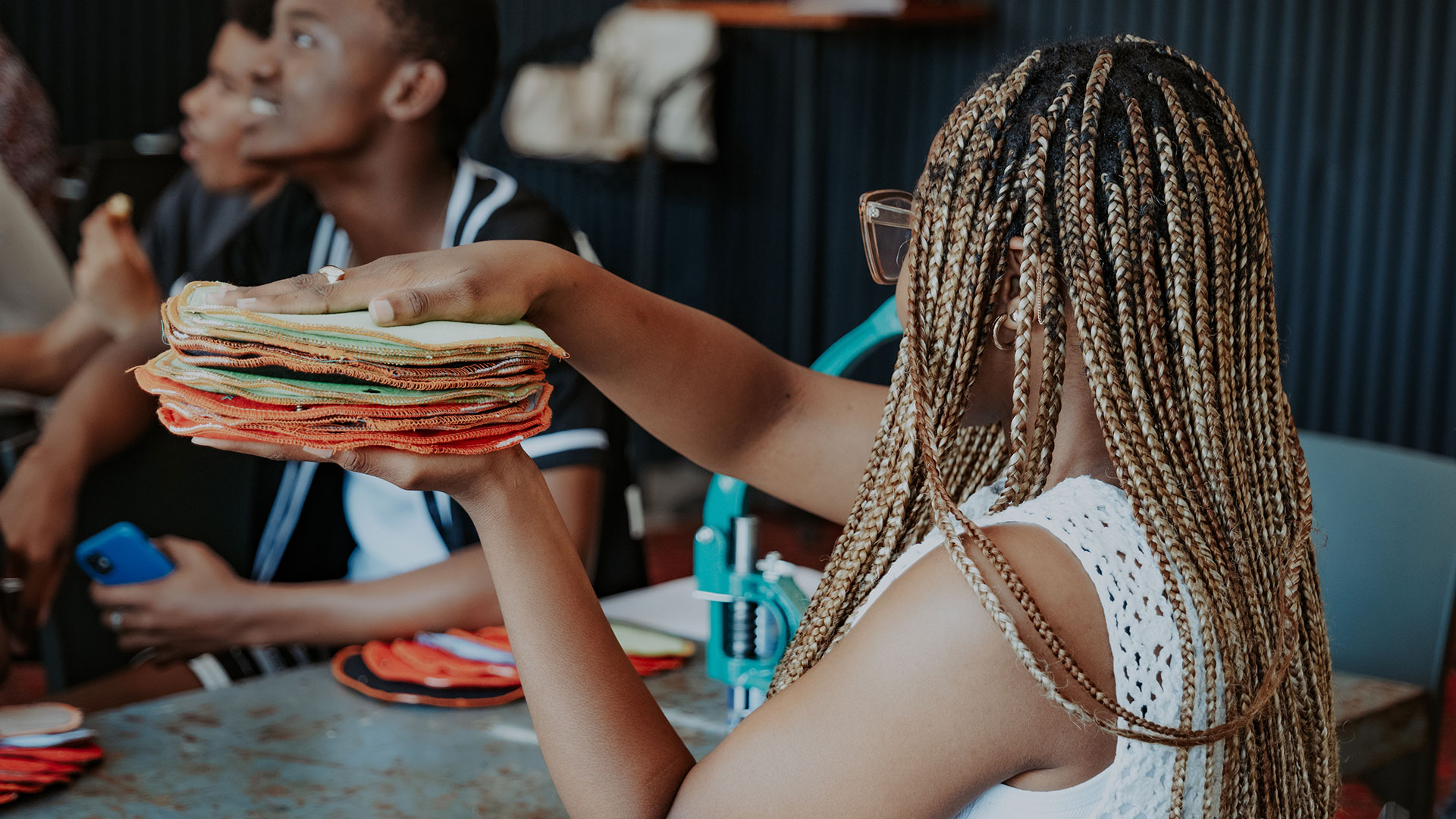 Young volunteer passing a pile of stitched sanitary pads to her sewing partner.