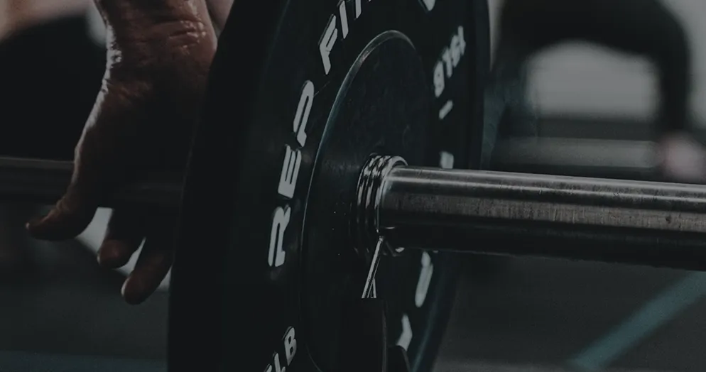 Close-up of a hand gripping a barbell with weight plates in a gym setting.