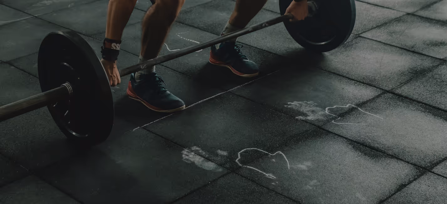 Person preparing to lift a loaded barbell on gym floor marked with chalk handprints.