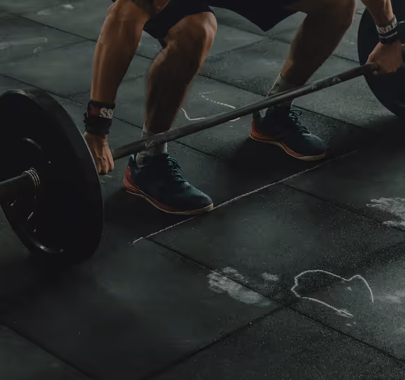Person gripping a barbell on a gym floor marked with white chalk lines and handprints.