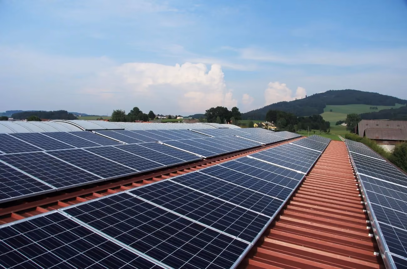 Ein Dach voller Solarmodule an einem sonnigen Tag, mit grünen Hügeln im Hintergrund.