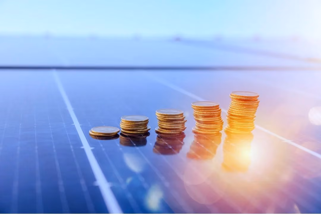 Münzstapel auf einer Solaranlage, auf die die Sonne scheint.