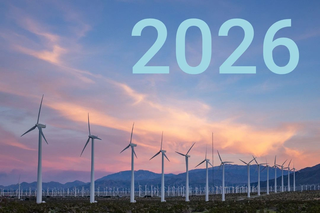 Viele Windkraftanlagen stehen vor einem Bergzug, im Hintergrund geht die Sonne auf.