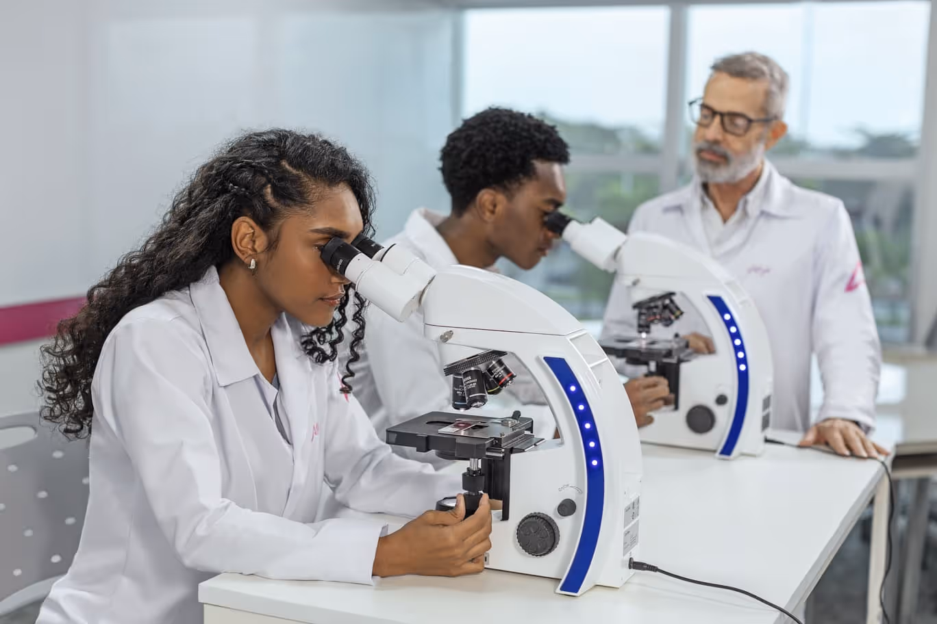 Alunos usando um microscópio no laboratório sob a supervisão do professor