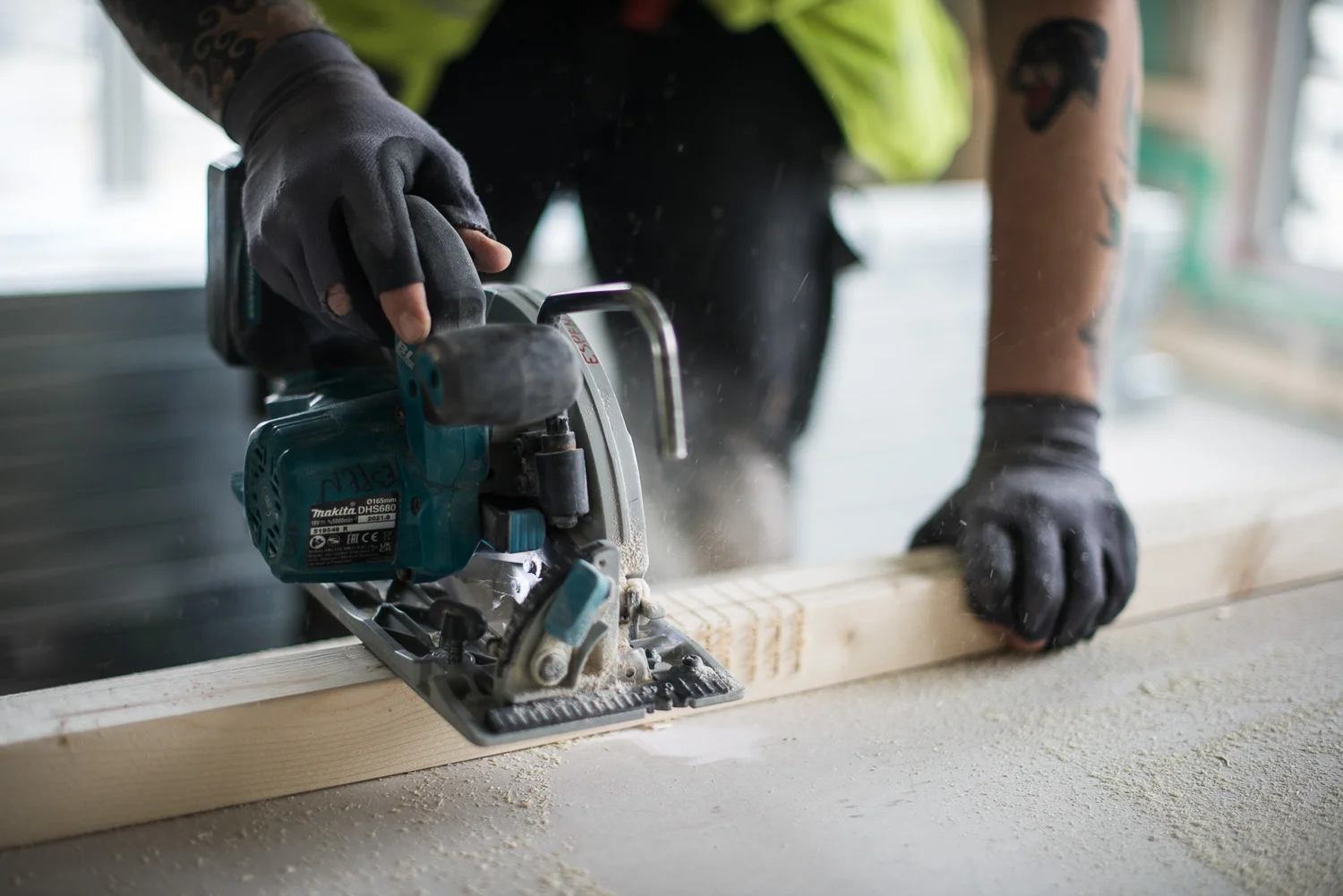 Person wearing gloves using a circular saw to cut a wooden plank on a workbench.