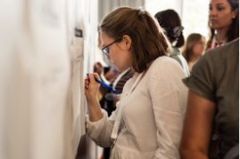 A woman is writing on a board during a collaborative session, with others participating in the background.