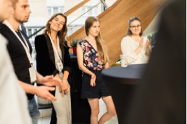 A group of people stand around a table, attentively listening during a casual discussion or meeting.
