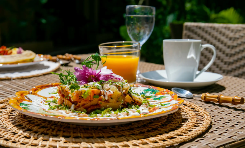 Brunch al aire libre con un platillo colorido, jugo, café y ambiente soleado.