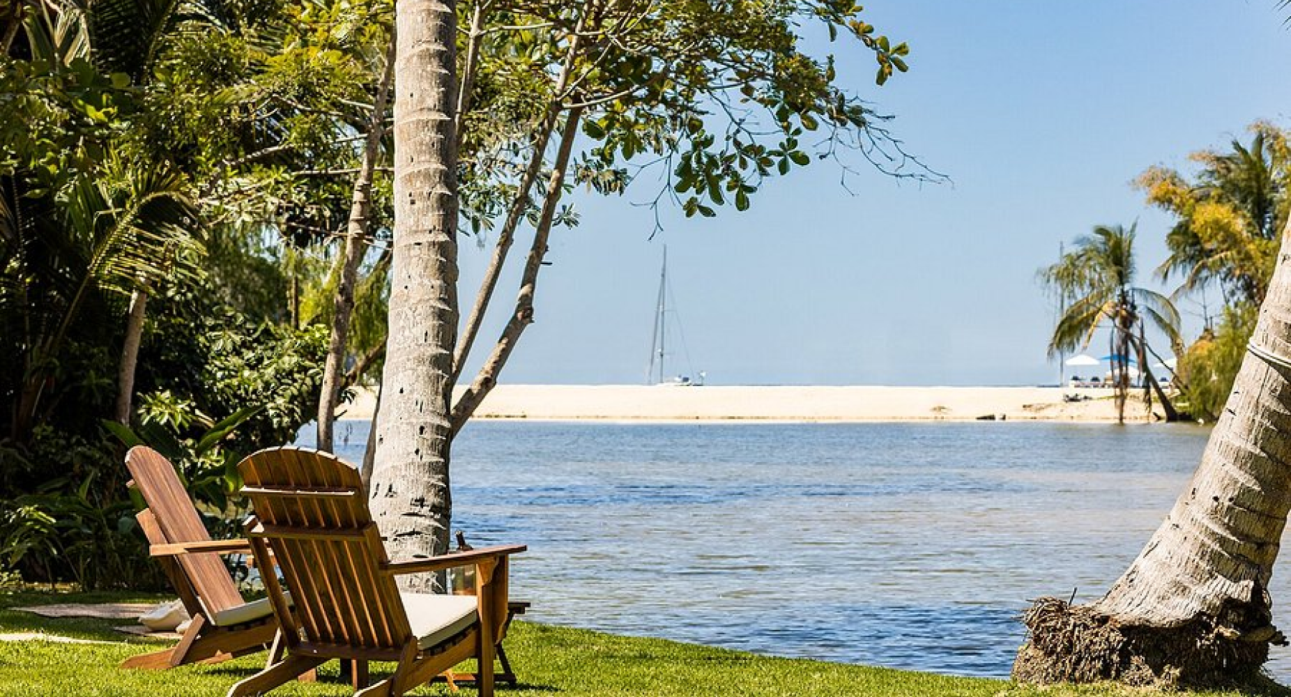 Two lounge chairs facing tropical waters, surrounded by palm trees and greenery.