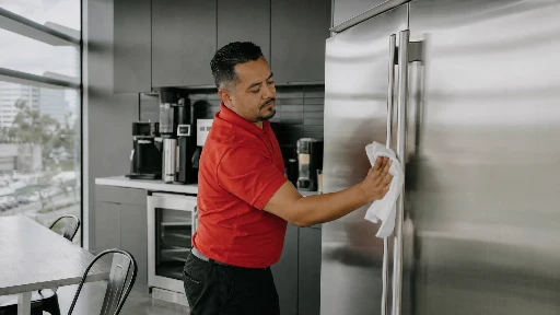 Commercial cleaning technician in red polo sanitizing stainless steel appliances in a Los Angeles Class A office break room