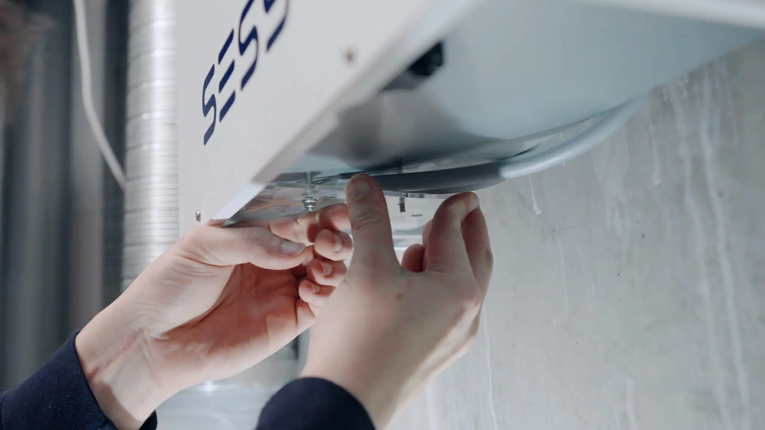 Een monteur die een wit apparaat met het label Sessy aan de muur bevestigd.