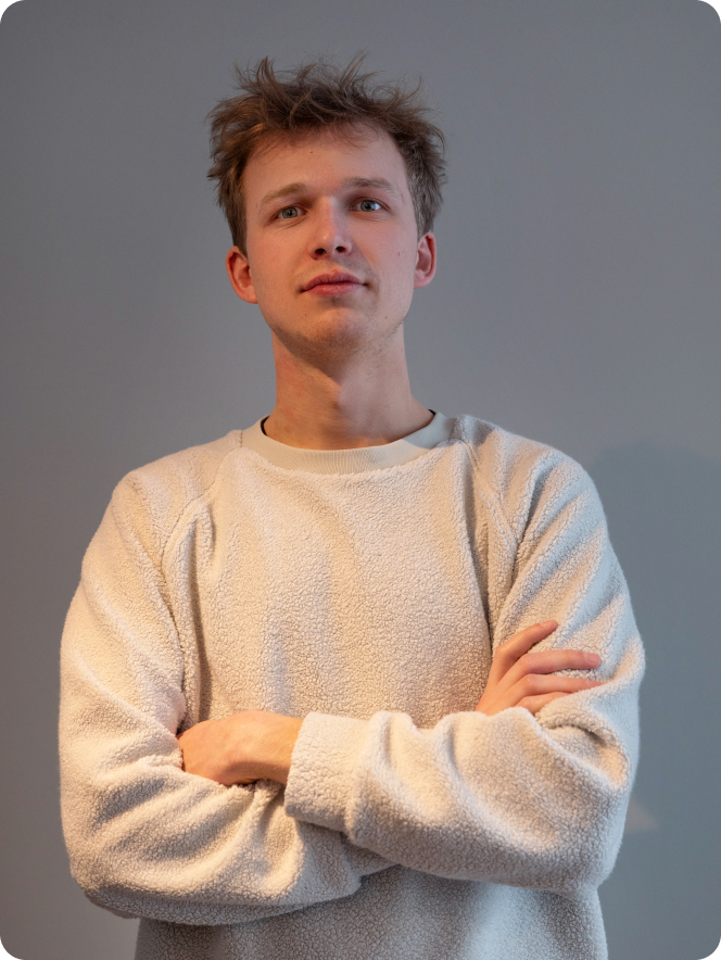 A man with a beard and curly hair wearing a grey sweater.