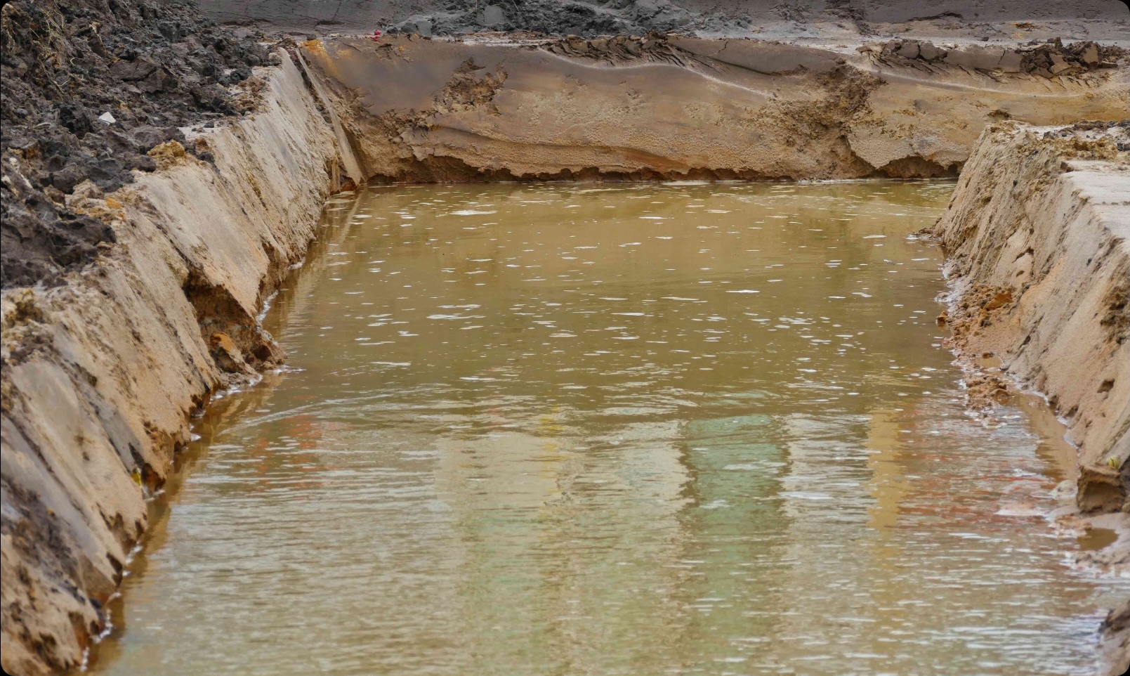 A muddy pond with a reflection of a building.