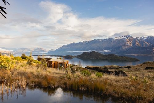 a building on a mountain side overlooking a lake with mountains in the background