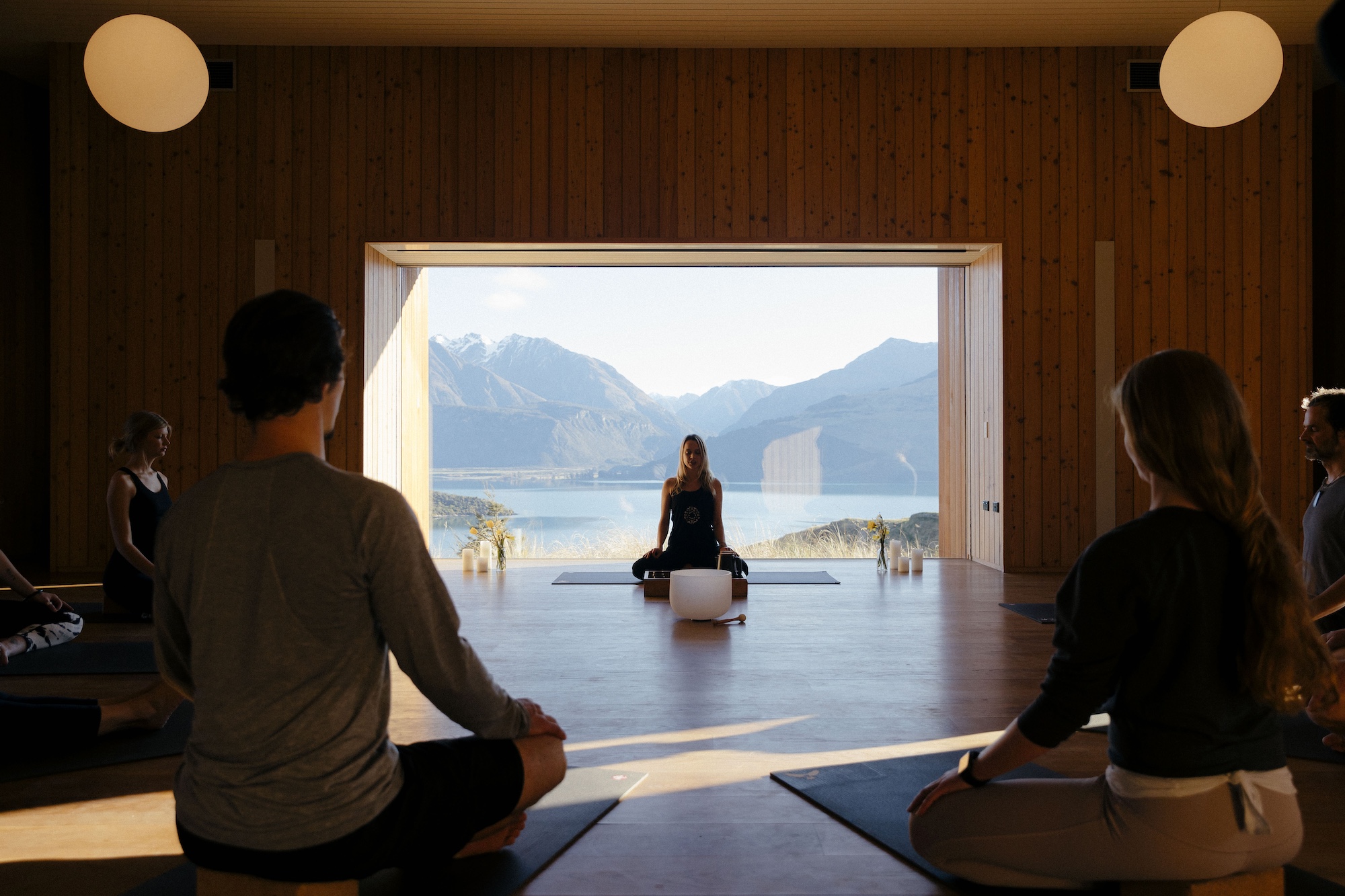looking into a dimly lit yoga room where a woman is sitting on a yoga mat with a beautiful mountain backdrop of of the window behind her