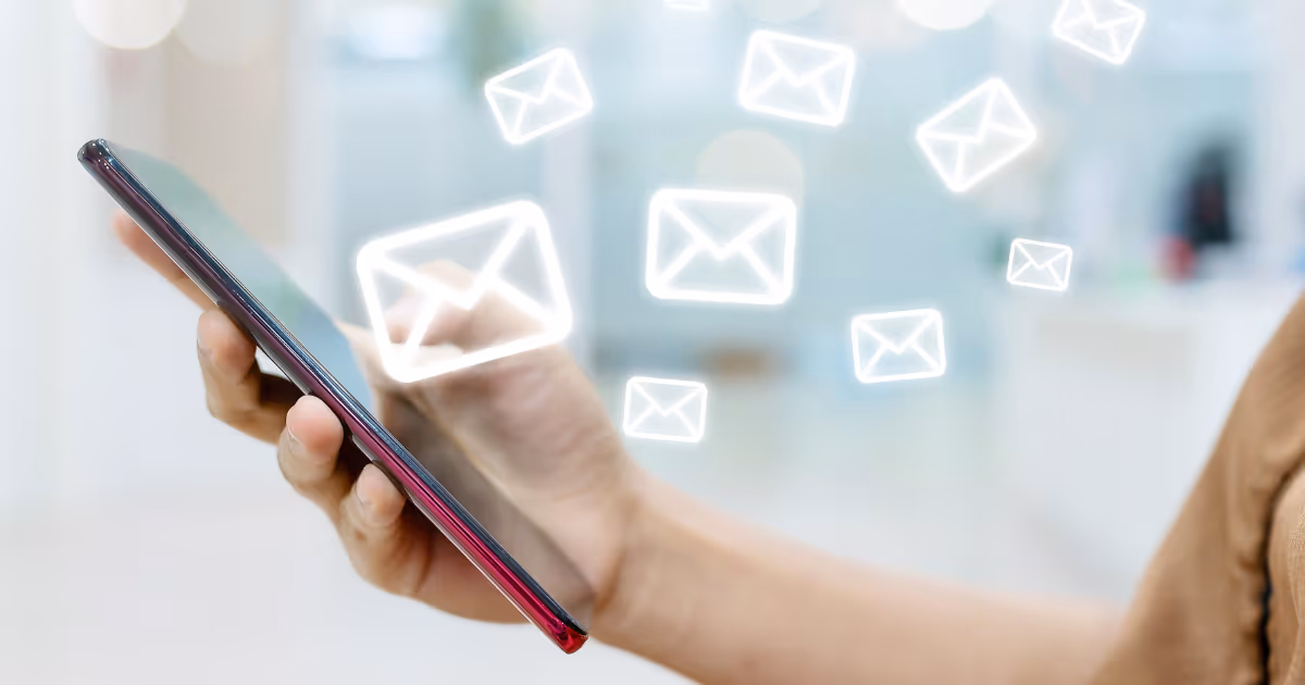 Person holding a cell phone with email icons floating above it.
