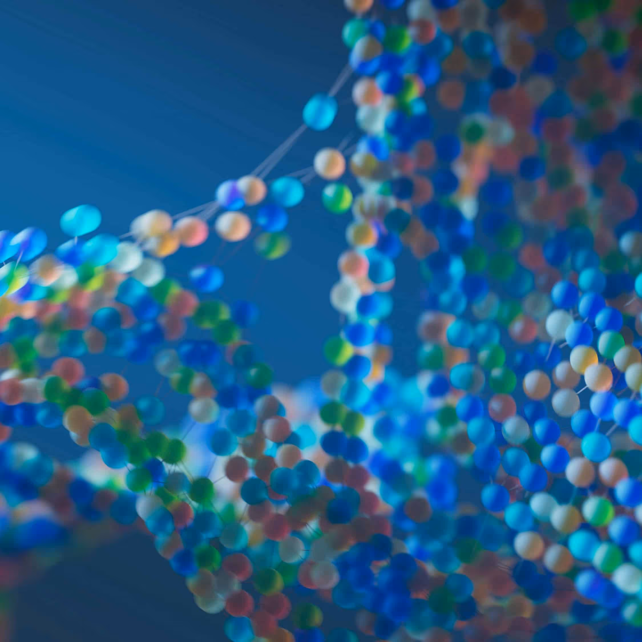 Abstract close-up of a colorful, blurred molecular structure with interconnected spheres in blue, green, and pastel tones against a soft blue background.