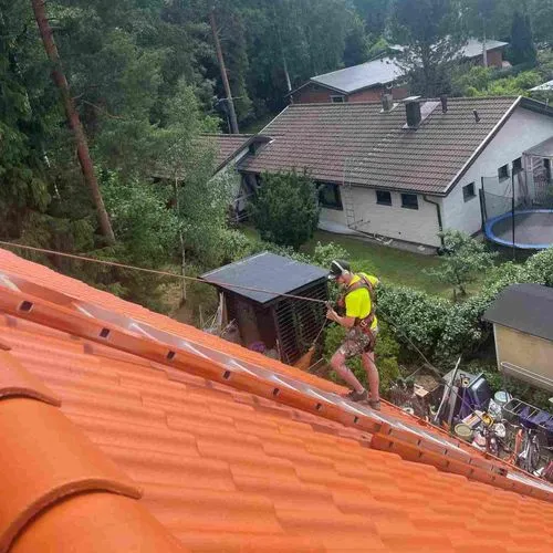 Maalari maalaamassa jyrkkää tiilikattoa