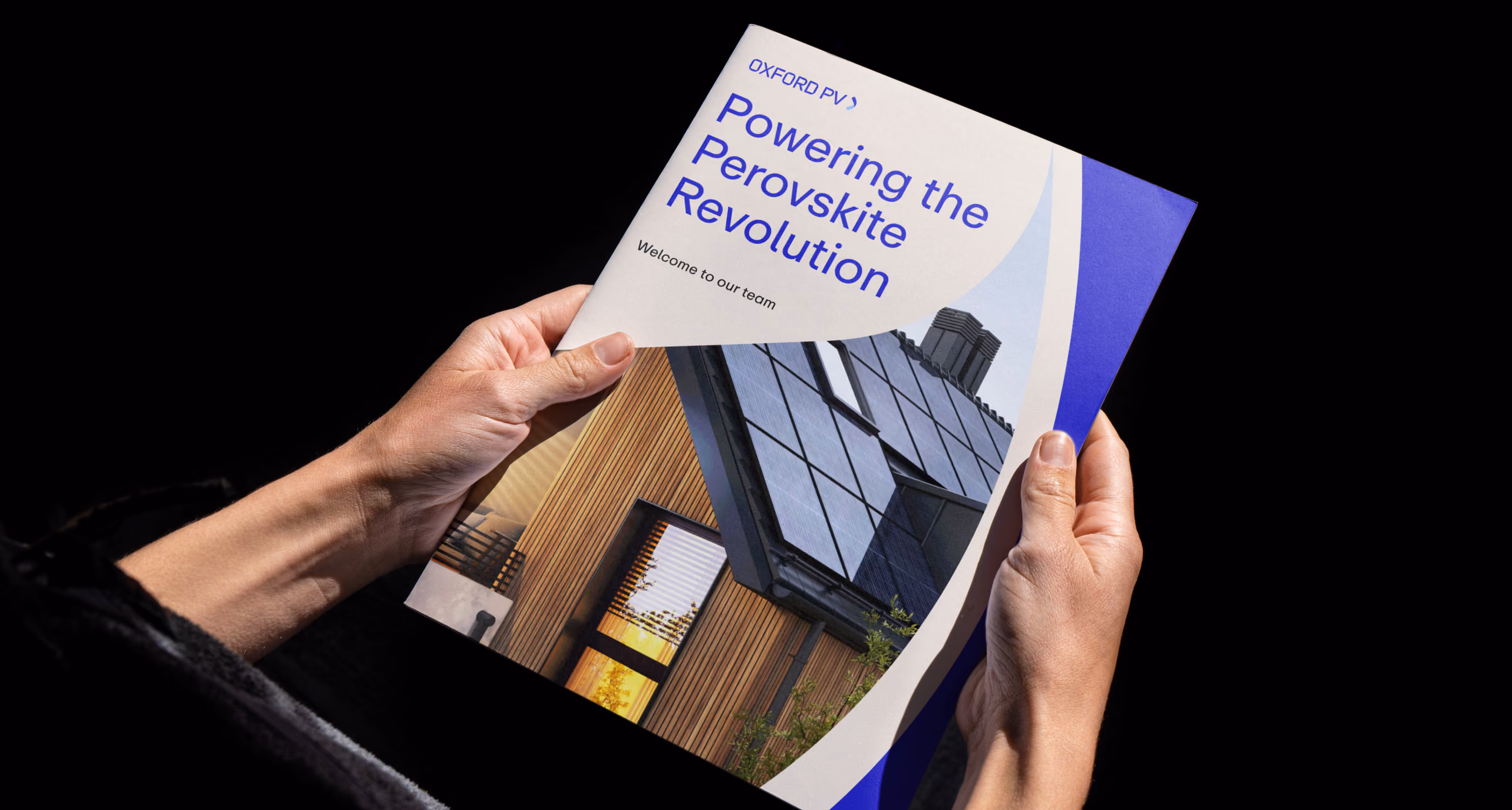 Hands holding brochure titled 'Powering the Perovskite Revolution' featuring solar panels on a modern house roof.