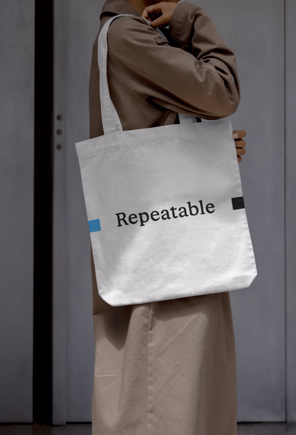 Person in brown coat carrying white tote bag with the word 'Repeatable' printed on it.