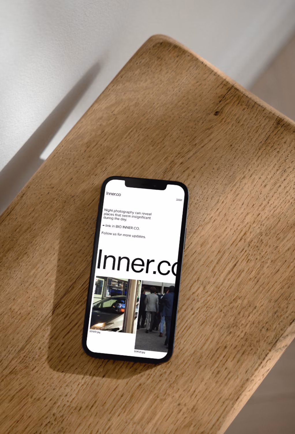 Smartphone on a wooden table displaying Inner.co website about night photography and a car and group photo.