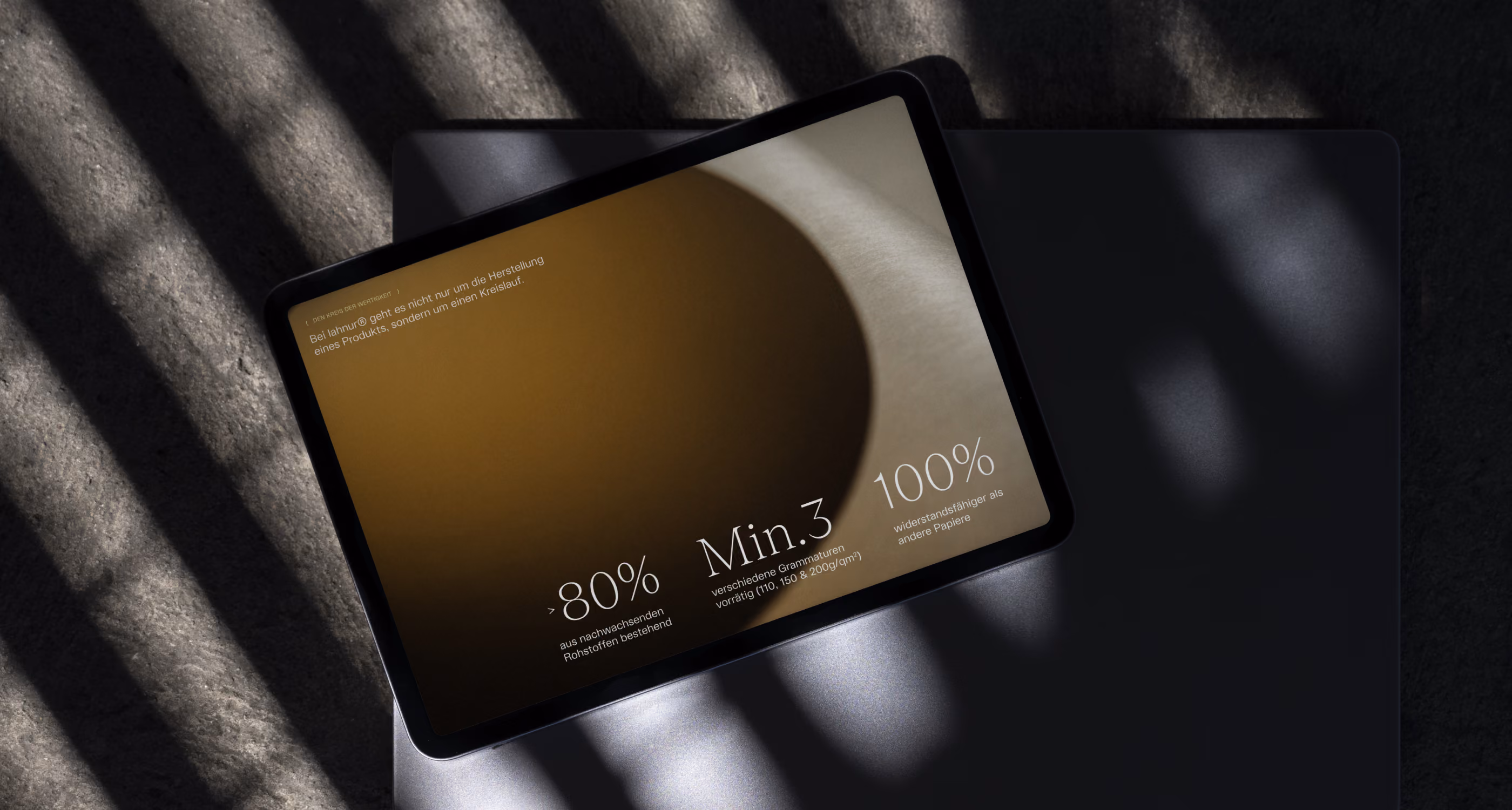 Tablet displaying text with statistics about sustainable paper materials on a textured surface with shadows.