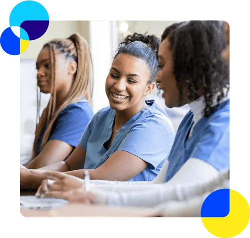 A group of women in medical scrubs sitting together at a table, engaged in a professional discussion.